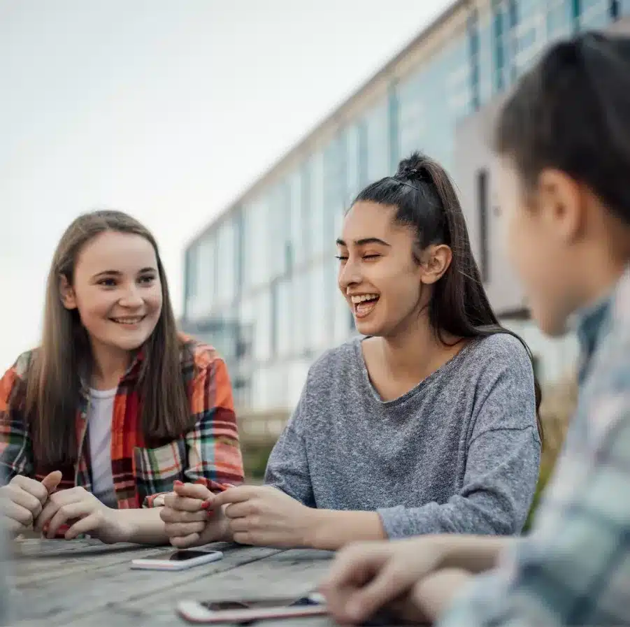 trois jeunes filles rient ensemble a une table en bois devan